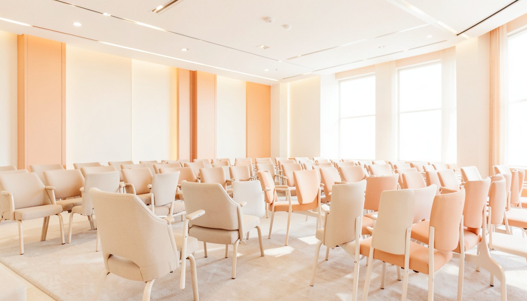 Bright, airy photograph of a modern conference venue interior with warm lighting, neutral tones, and rows of seating arranged for a formal event